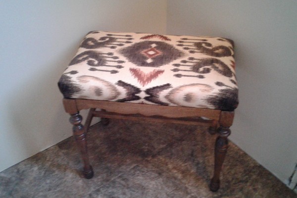 A wood frame stool with an upholstered patterned seat