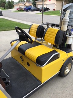 A yellow golf cart with custom black and yellow seating