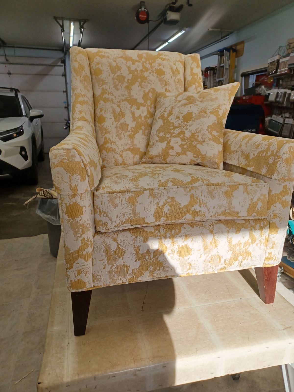 A wingback armchair and matching cushion in yellow and cream patterned fabric