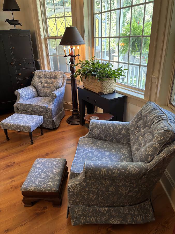 Two armchairs and two footstools upholstered in matching blue-grey botanical fabric beside tall windows